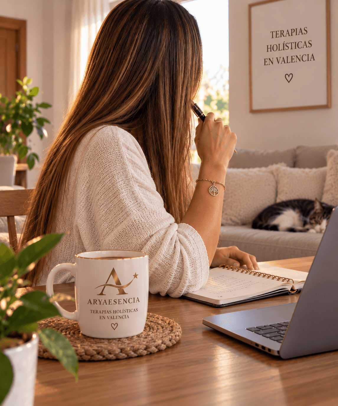 Mujer escribiendo en un cuaderno junto a una taza de terapias holísticas y un portátil.